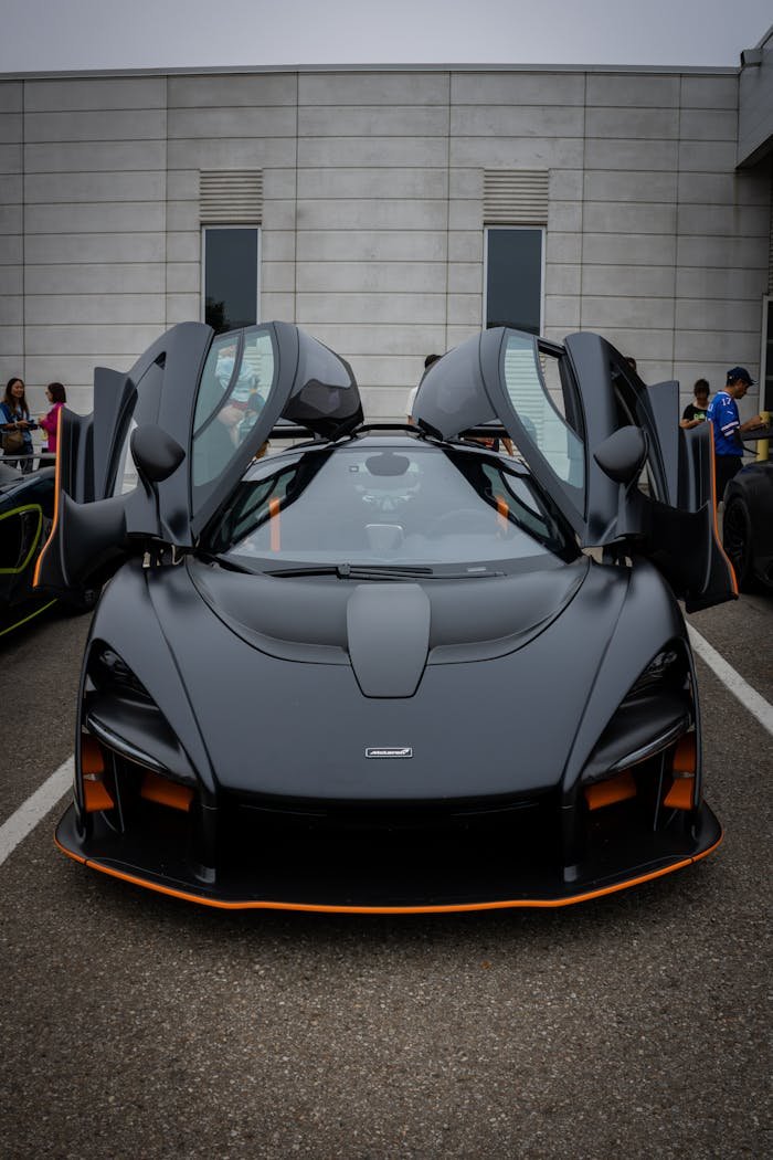Front view of a luxury sports car with butterfly doors open in a parking lot.