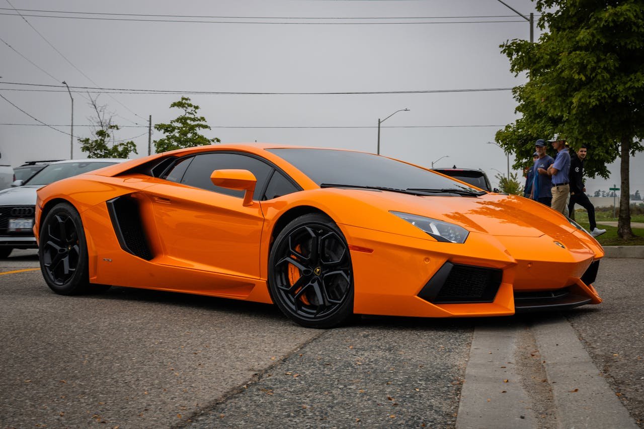 Eye-catching orange sports car on a street with people nearby, showcasing luxury design.